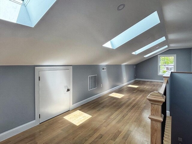 additional living space featuring a skylight, vaulted ceiling, wood finished floors, and baseboards