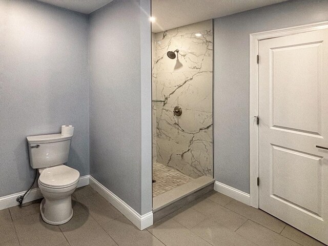 bathroom featuring toilet, a marble finish shower, and baseboards