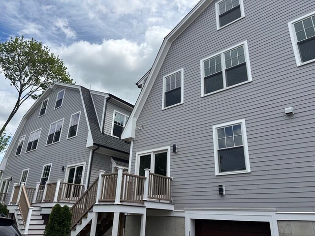 back of property featuring a gambrel roof, a wooden deck, an attached garage, and stairs