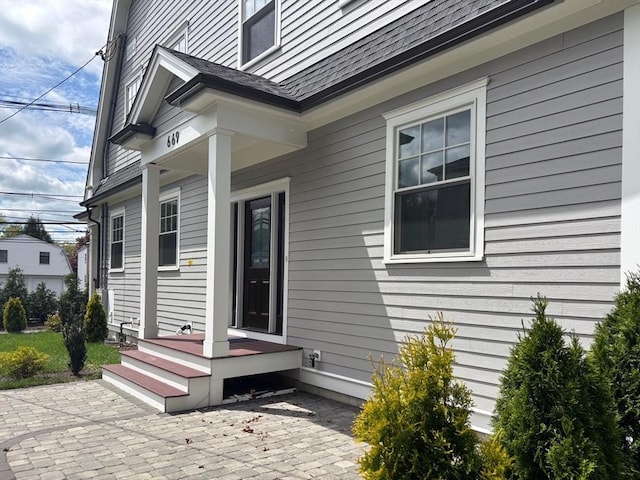 property entrance featuring a patio and a shingled roof