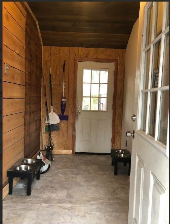 mudroom with wood walls, wooden ceiling, concrete flooring, and vaulted ceiling