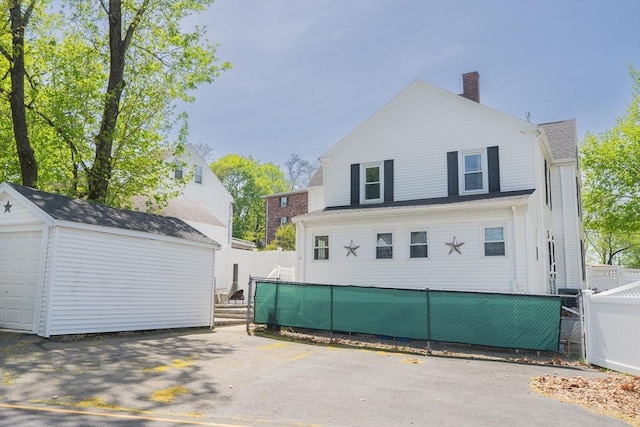 rear view of property with a garage, an outbuilding, fence private yard, and a chimney