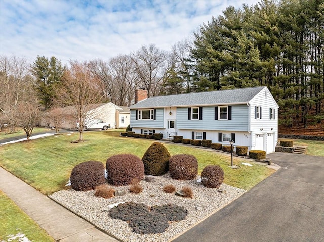 bi-level home with a front yard, a garage, driveway, and a chimney