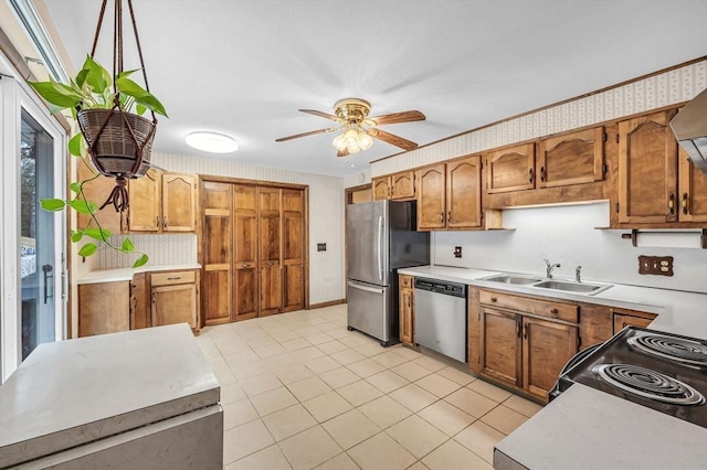 kitchen with ceiling fan, light countertops, brown cabinetry, stainless steel appliances, and a sink