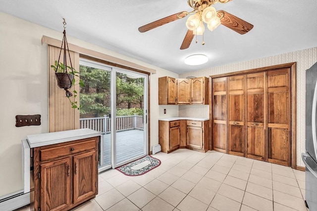 kitchen featuring light tile patterned flooring, brown cabinetry, light countertops, baseboard heating, and ceiling fan