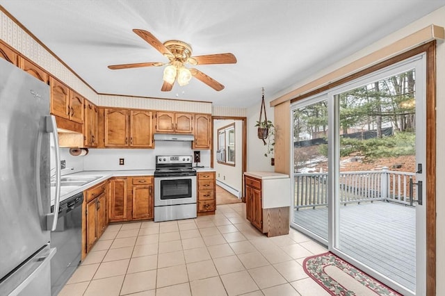 kitchen with a sink, under cabinet range hood, light countertops, appliances with stainless steel finishes, and a baseboard radiator