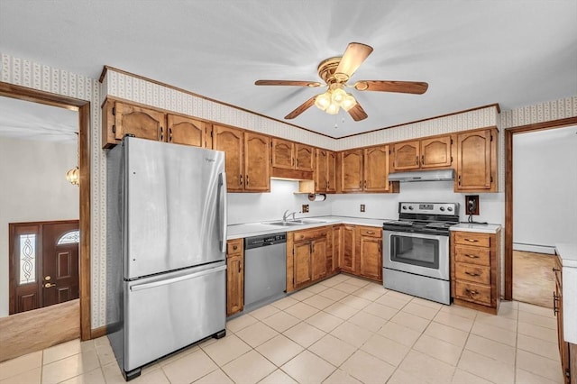 kitchen with brown cabinets, under cabinet range hood, a sink, appliances with stainless steel finishes, and wallpapered walls