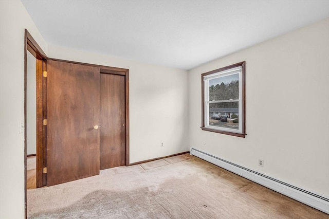 unfurnished bedroom with a closet, baseboard heating, light carpet, and baseboards