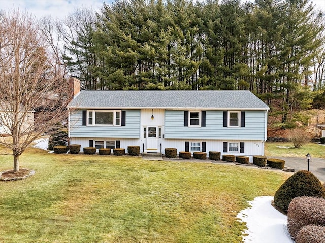 raised ranch with a front yard, a shingled roof, a chimney, and entry steps