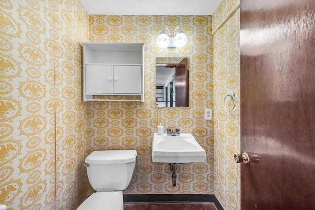 bathroom featuring a sink, toilet, and wallpapered walls