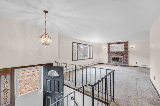 stairs with an inviting chandelier, a brick fireplace, carpet, and a baseboard radiator