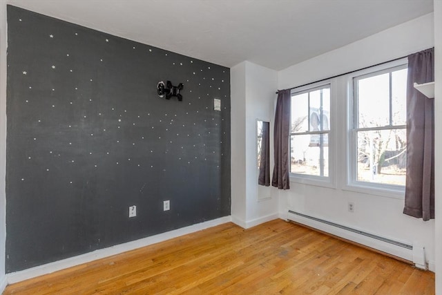 empty room with light wood finished floors, baseboard heating, an accent wall, and baseboards