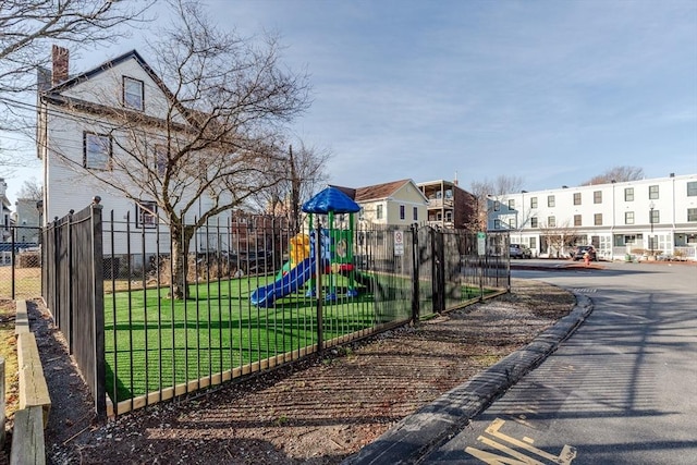 community play area featuring fence, a lawn, and a residential view