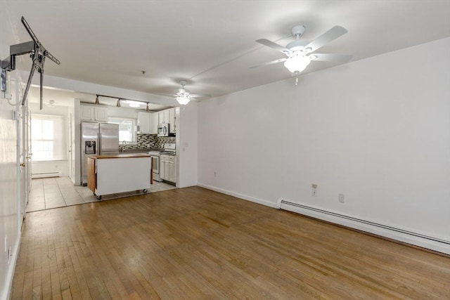 kitchen with a baseboard heating unit, white appliances, white cabinets, light wood finished floors, and decorative backsplash