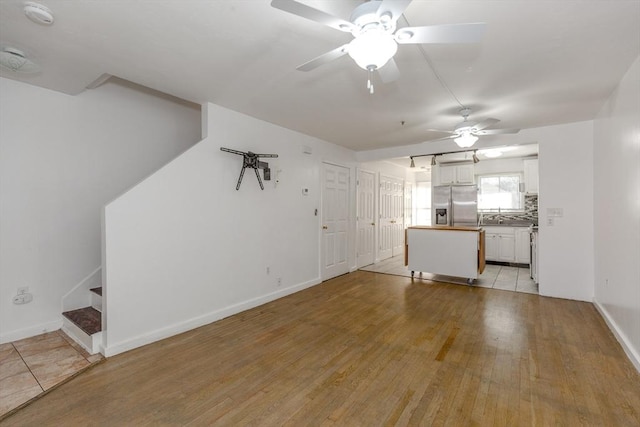 unfurnished living room featuring stairway, baseboards, a sink, ceiling fan, and light wood-type flooring