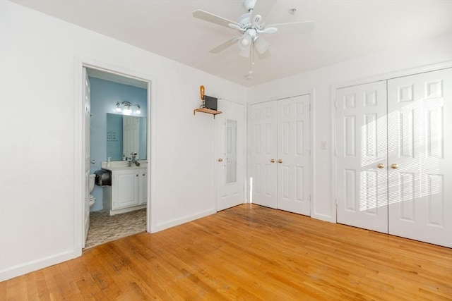 unfurnished bedroom with ensuite bathroom, light wood-style floors, baseboards, and two closets