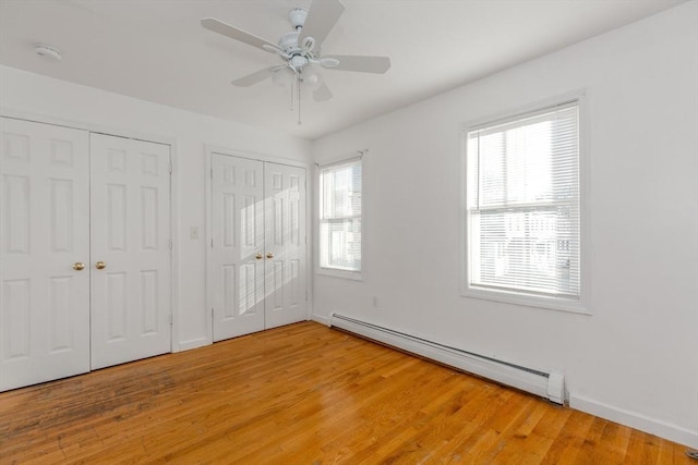 unfurnished bedroom featuring baseboard heating, light wood-style flooring, two closets, and baseboards