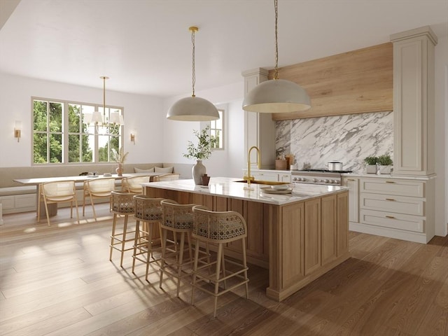 kitchen with decorative light fixtures, light stone counters, light hardwood / wood-style floors, tasteful backsplash, and a kitchen island with sink