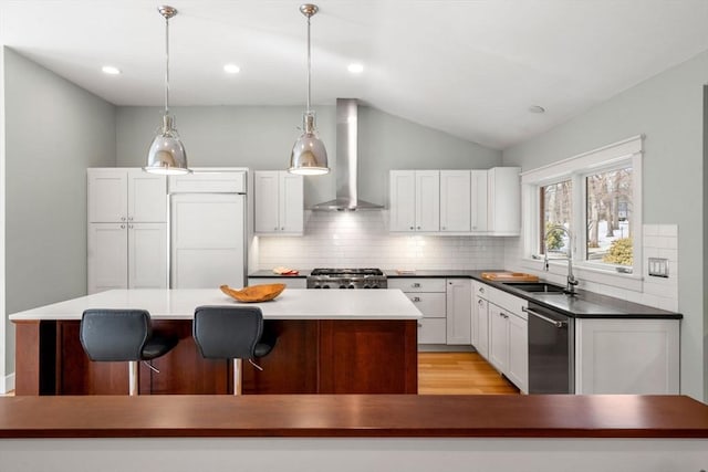 kitchen with a center island, stainless steel dishwasher, a sink, wall chimney range hood, and range