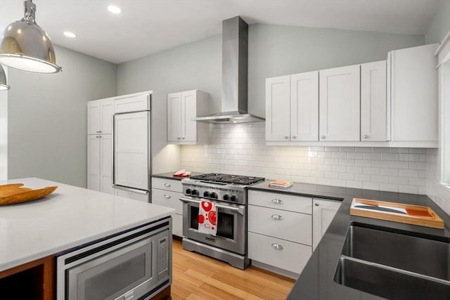 kitchen featuring decorative backsplash, a sink, built in appliances, light wood-type flooring, and wall chimney exhaust hood