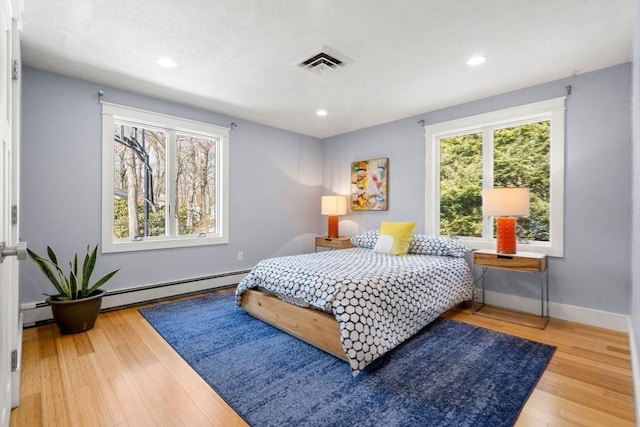 bedroom featuring wood finished floors, visible vents, baseboard heating, and multiple windows