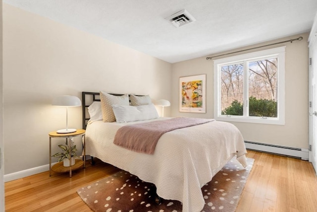 bedroom featuring baseboards, visible vents, baseboard heating, and wood finished floors