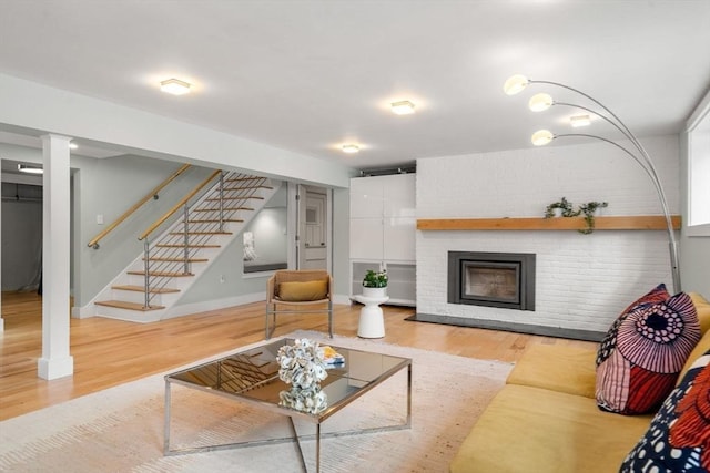 living area featuring stairway, a brick fireplace, wood finished floors, and baseboards