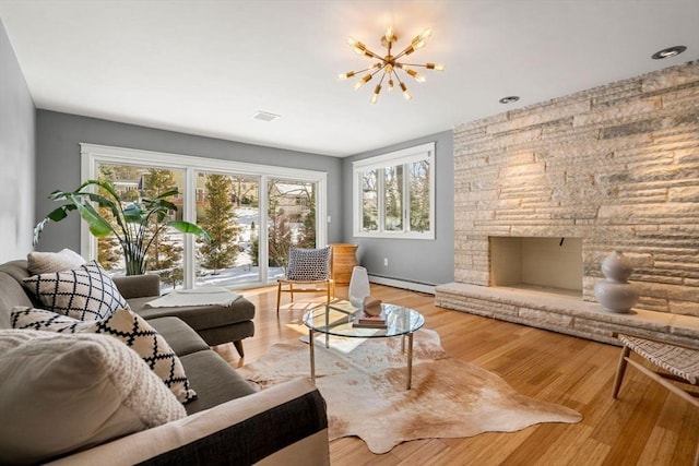 living room with a notable chandelier, a fireplace, baseboard heating, and wood finished floors