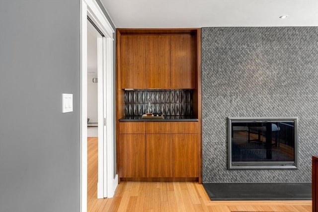 interior space featuring light wood finished floors, brown cabinetry, dark countertops, modern cabinets, and a fireplace