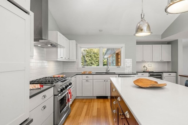 kitchen with beverage cooler, a sink, high end stainless steel range, light wood-type flooring, and wall chimney exhaust hood