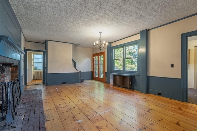 unfurnished living room featuring radiator heating unit, hardwood / wood-style flooring, a textured ceiling, and a chandelier