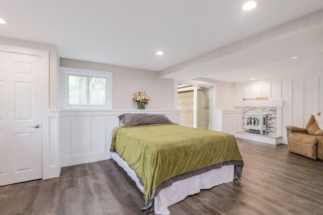 bedroom featuring a decorative wall, wood finished floors, recessed lighting, a fireplace with raised hearth, and a wainscoted wall