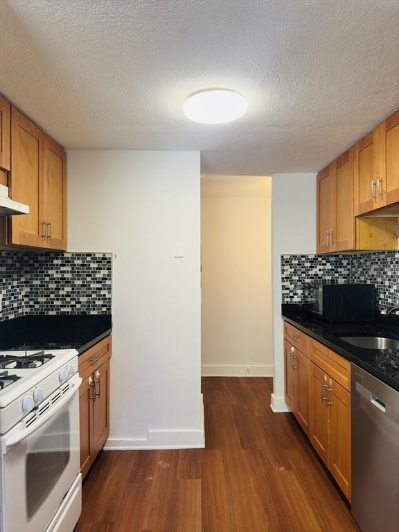 kitchen featuring stainless steel dishwasher, dark hardwood / wood-style floors, gas range gas stove, backsplash, and sink