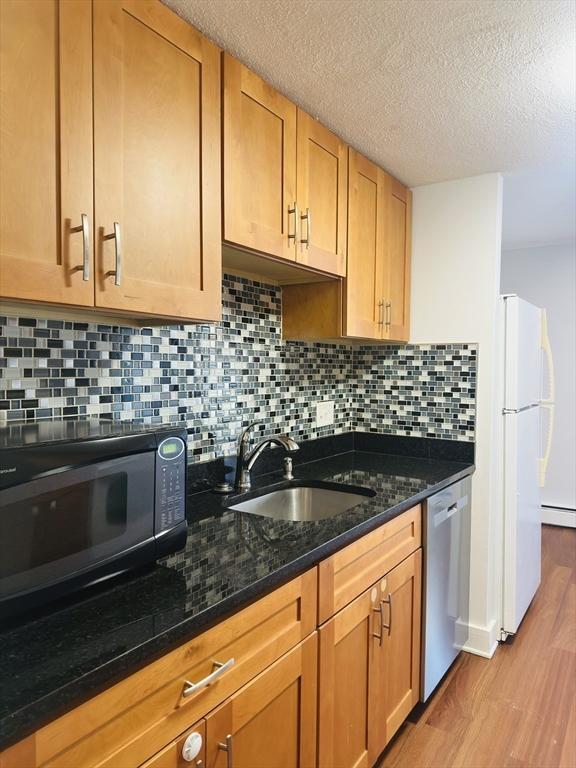 kitchen with white refrigerator, sink, dark stone countertops, stainless steel dishwasher, and backsplash