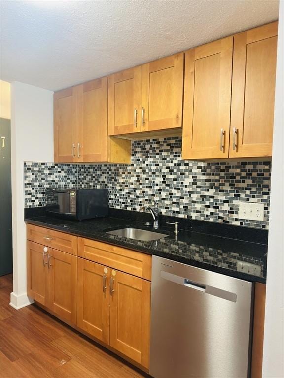 kitchen featuring dishwasher, wood-type flooring, dark stone counters, sink, and tasteful backsplash