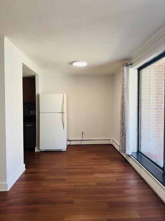 unfurnished room with a wealth of natural light, a textured ceiling, a baseboard heating unit, and dark hardwood / wood-style flooring