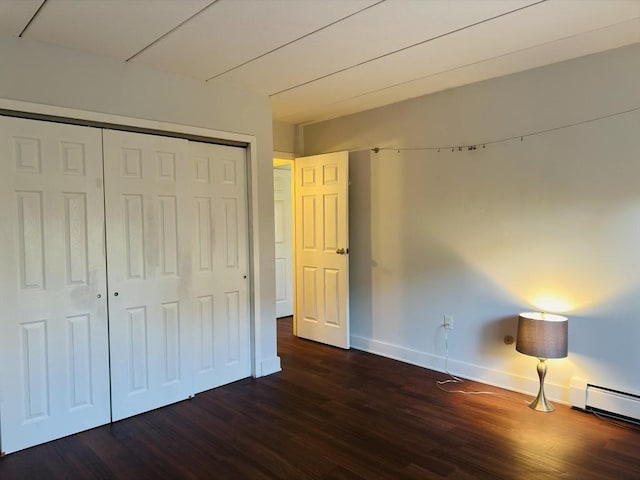 unfurnished bedroom featuring a baseboard heating unit, a closet, and dark hardwood / wood-style flooring