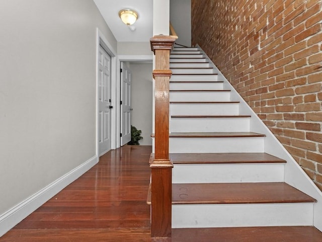 staircase with wood finished floors, baseboards, and brick wall