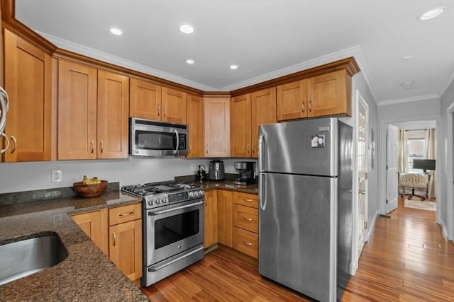 kitchen with appliances with stainless steel finishes, light wood-type flooring, dark stone countertops, brown cabinetry, and recessed lighting