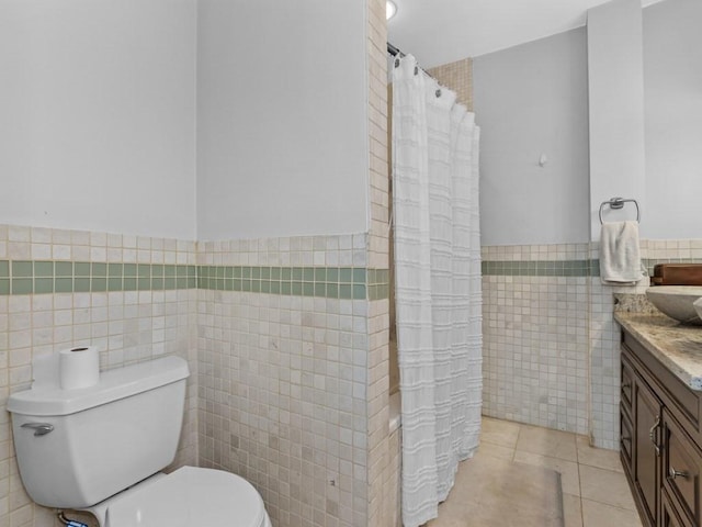 full bath with tile walls, tile patterned flooring, toilet, vanity, and wainscoting