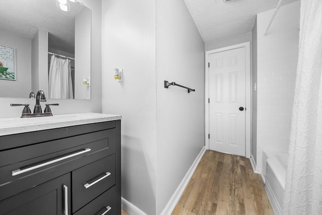 full bathroom featuring vanity, wood finished floors, baseboards, a textured ceiling, and shower / tub combo