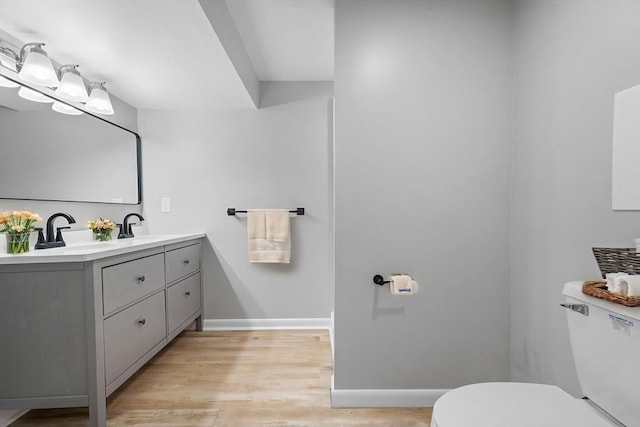 bathroom with double vanity, wood finished floors, a sink, baseboards, and toilet