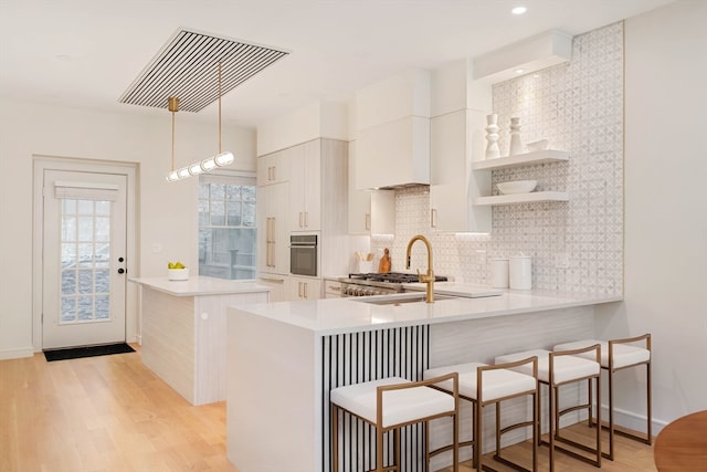 kitchen featuring oven, light hardwood / wood-style floors, hanging light fixtures, and kitchen peninsula