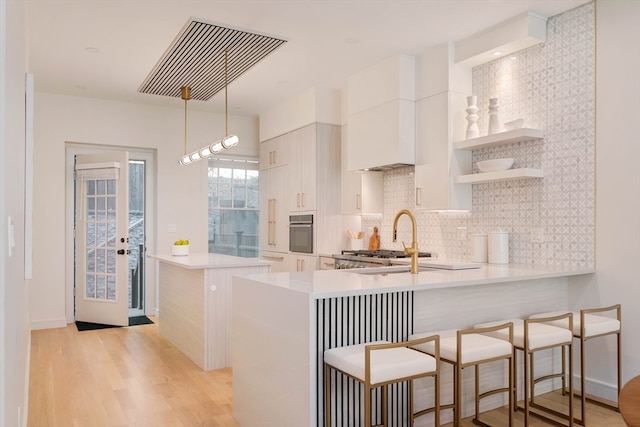 kitchen with pendant lighting, kitchen peninsula, light hardwood / wood-style flooring, stainless steel oven, and a kitchen bar