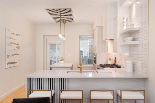 kitchen featuring white cabinets, kitchen peninsula, decorative light fixtures, a breakfast bar area, and light hardwood / wood-style floors