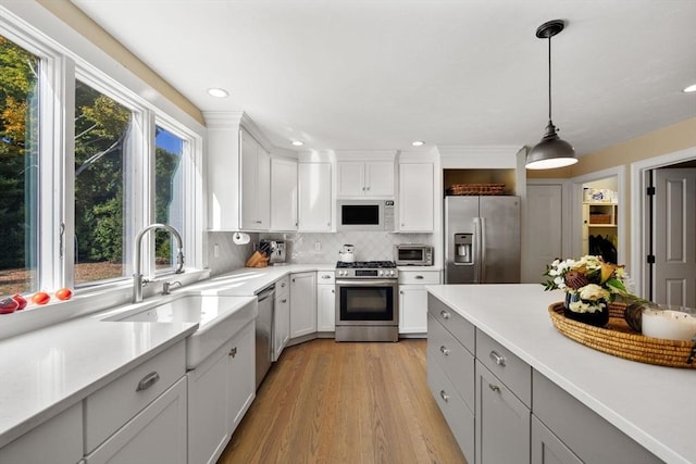 kitchen featuring sink, light hardwood / wood-style floors, pendant lighting, white cabinets, and appliances with stainless steel finishes