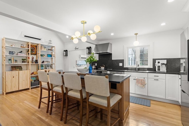 173 Liberty St, Braintree, MA 02184 - kitchen featuring wall chimney range hood, dark countertops, a kitchen island, decorative backsplash, and light wood-style floors
