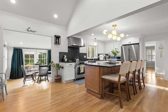 173 Liberty St, Braintree, MA 02184 - kitchen with wall chimney exhaust hood, appliances with stainless steel finishes, dark countertops, a kitchen island, and white cabinets