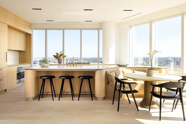 kitchen with a breakfast bar area, a sink, light brown cabinetry, stainless steel oven, and modern cabinets