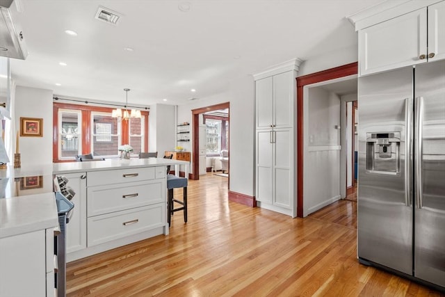 kitchen with visible vents, light countertops, light wood-style flooring, stainless steel refrigerator with ice dispenser, and white cabinets